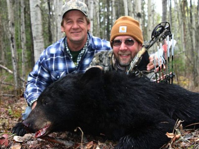 Outfitter and hunter joking as they squat behind Brent\'s bear for a photo. This bear was taken on a baited hunt off an active bait barrel loaded with our own secret recipe of bear foods. This trophy is one of two bears my hunter shot at with his bow. An excellent shot and a great hunter to have in camp.
